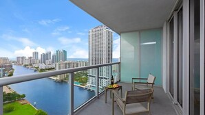 A balcony with a view of a river and cityscape, a table with a bottle and food, and a chair. - Beachside Stay | Infinite View | Balcony | Miami (Hallandale Beach)