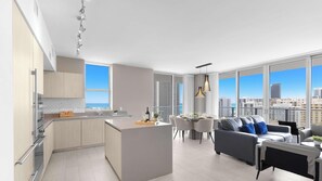 A modern apartment with a kitchen, dining area, and living room, featuring large windows with city views. - Spectacular View 2BR | Pools & Relax (Hollywood)