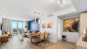 A modern living room with a dining area, large windows, and a city view. - Cozy Upper Apartment | Bay View Fitness Center (Hallandale Beach)