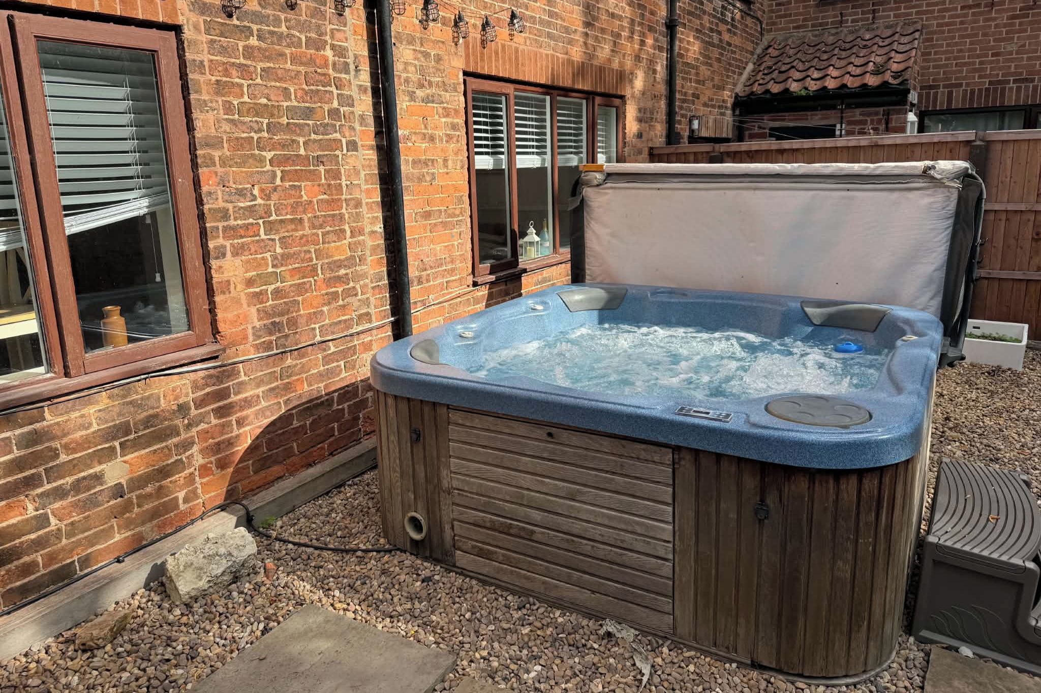 Un jacuzzi en un patio trasero con un muro de ladrillo, una terraza de madera y una ventana.