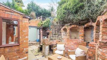 A brick building with a patio area featuring wicker furniture and a brick oven.