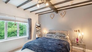 Un dormitorio con una cama grande, una mesita de noche, cortinas en la ventana y vigas a la vista en el techo.