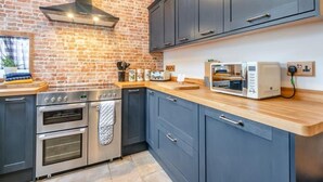 Una cocina con pared de ladrillo, armarios oscuros, horno empotrado y microondas en la encimera.