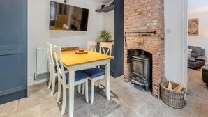 Un comedor con chimenea de ladrillo, un televisor montado en la pared y una disposición de asientos con sillas y una mesa.