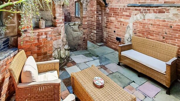 Un patio con mobiliario de mimbre, una mesa de piedra y un muro de ladrillo.