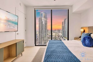A modern bedroom with a city view, a bed with a blue blanket, a wooden side table, and a TV mounted on the wall. - Amazing Apartment with amenities and Pool (Miami)