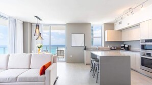 Eine moderne Küche mit einer zentralen Kochinsel, ein Essbereich mit einem weißen Sofa und Meerblick.