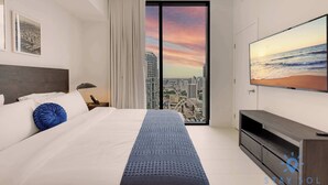 Ein modernes Hotelzimmer mit einem großen Bett, einem an der Wand befestigten Fernseher und Blick auf die Stadt durch das Fenster.