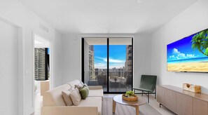 A modern living room with a sofa, a coffee table, a TV, and a view of a cityscape through large windows. - New! Stylish 1BR - Amenities & Pool (Miami)