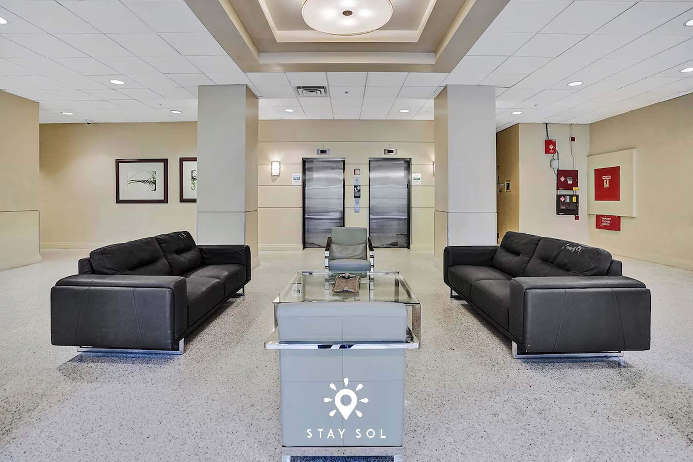 A lobby with two black sofas, a glass-top table, and a 'Stay Sol' sign.