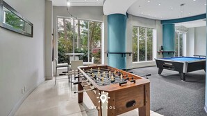 A modern indoor recreational area with a foosball table, a pool table, and large windows offering views of greenery. - Modern Hollywood Beach Escape - City Views (Hollywood)