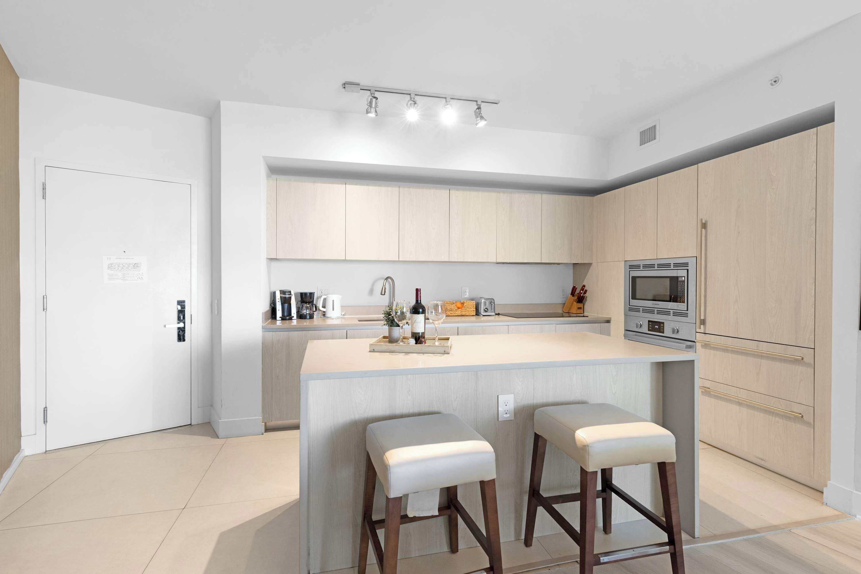 A modern kitchen with a central island, bar stools, and built-in appliances.