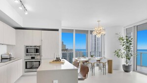 Cozinha moderna com ilha central, área de refeições com vista e uma grande planta em vaso.