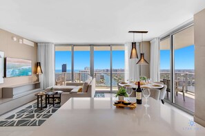 A modern living room with a large window, a dining area, and a sofa. - Luxury Hollywood Beach Condo w/Stunning Views (Hollywood)