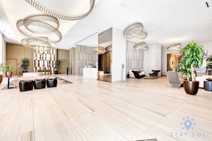 Een ruime lobby met een modern design, met een centraal zitgedeelte met een tafel en stoelen, een receptiebalie en decoratieve verlichtingsarmaturen.