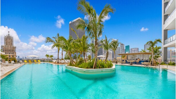Una piscina con palmeras, el horizonte de una ciudad y un edificio moderno.