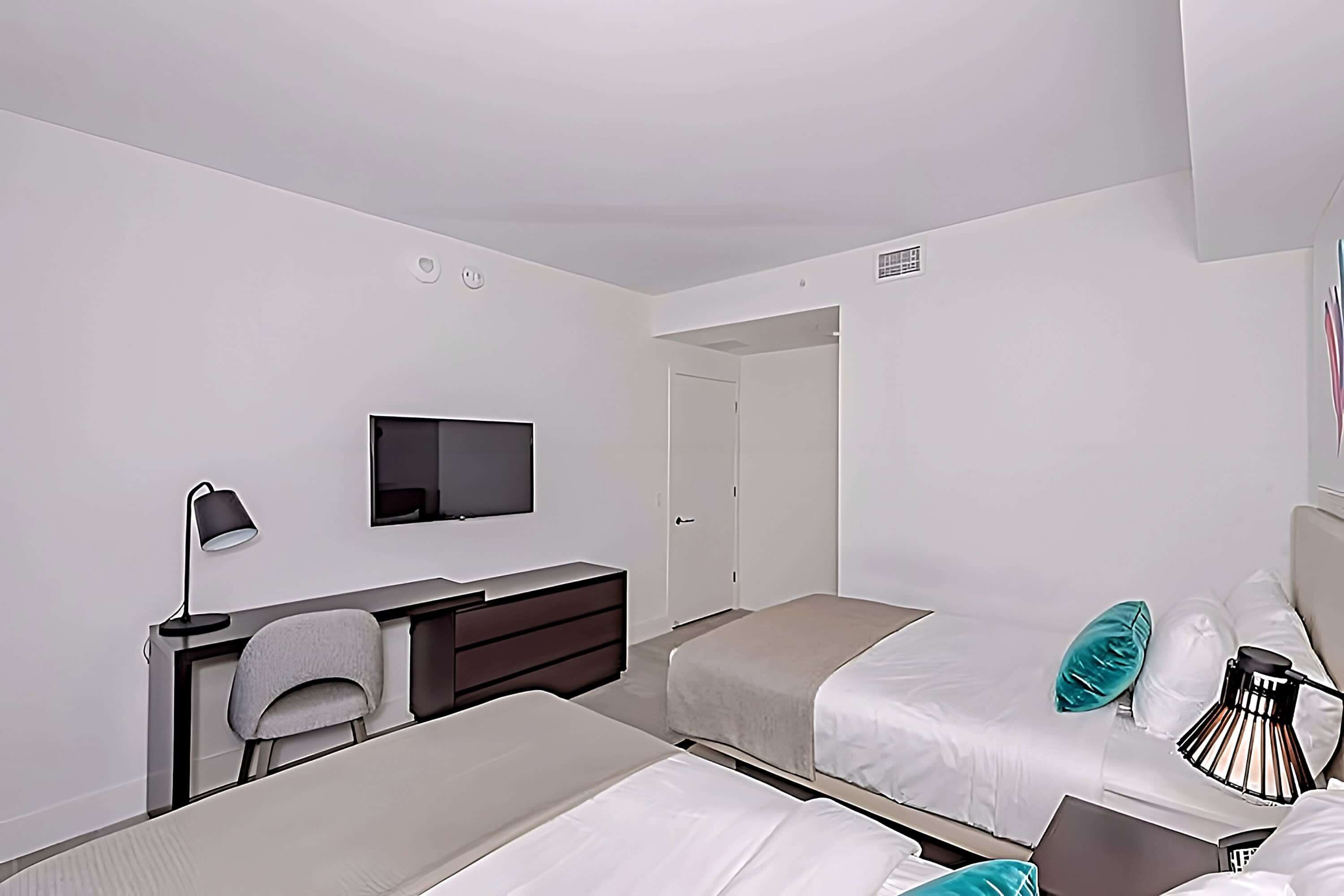 Ett hotellrum med två sängar, ett skrivbord med en stol, en TV och en lampa.