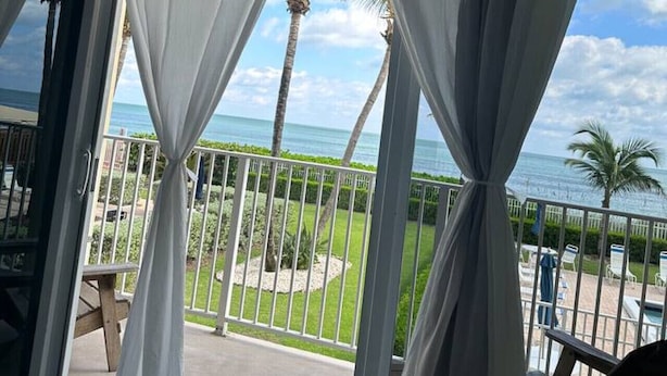Een kamer met uitzicht op de oceaan, een balkon met een leuning en een deur voorzien van gordijnen.