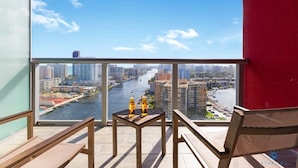 A balcony with a view of a river and cityscape, wooden furniture, and two bottles on a small table. - Stunning Infinity View Apt | Balcony & Pool (Hallandale Beach)