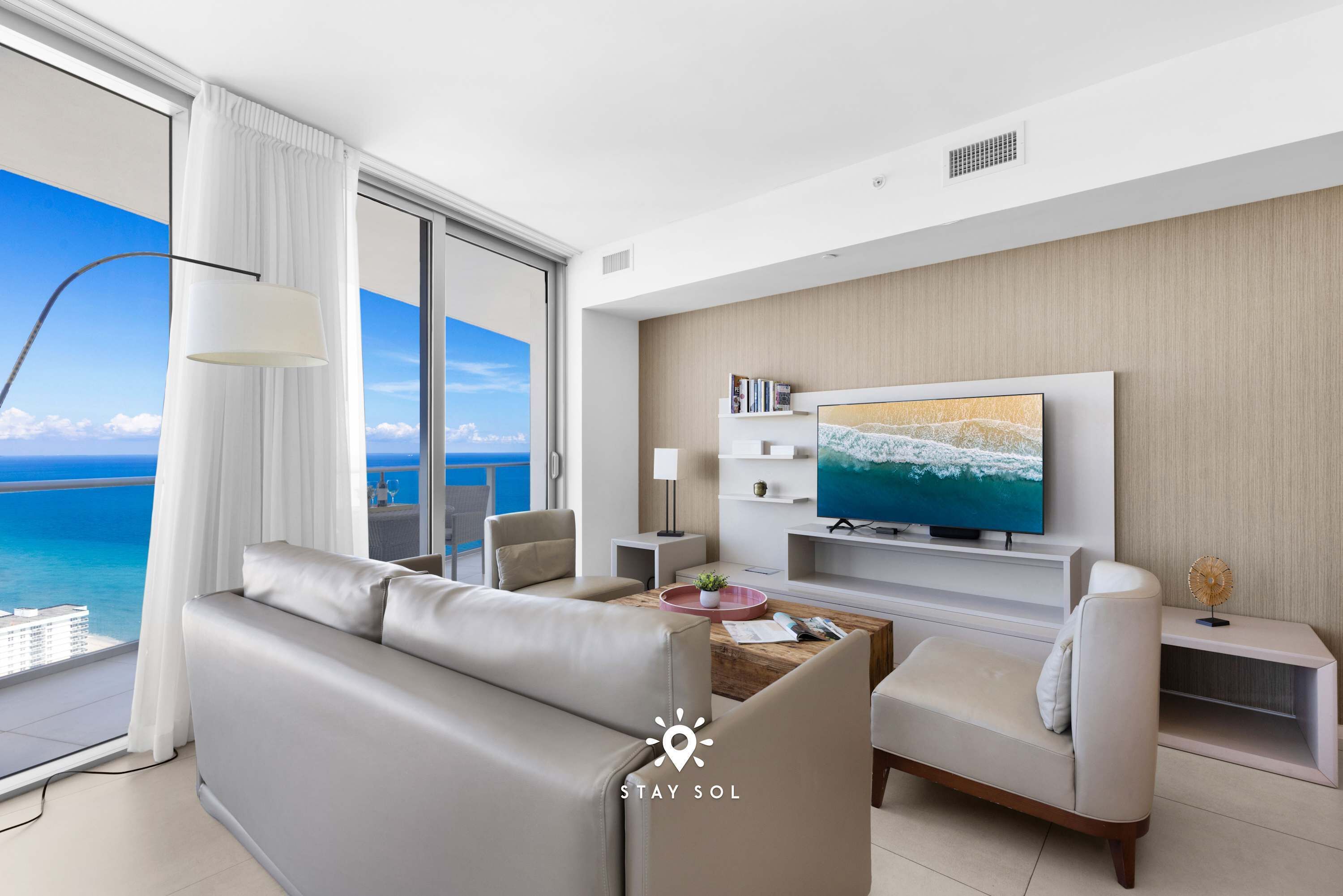 Una sala de estar moderna con un televisor grande, asientos cómodos y vistas al océano.