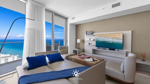 Et moderne hotelværelse med en stor seng, en sofa, et fjernsyn og udsigt til havet.
