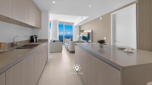 Et moderne køkken med en central ø, et spiseområde med udsigt og en opholdsstue med sofa og sofabord.
