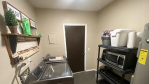 A laundry room with a washer and dryer, a microwave, and shelves with various items. - Lake Access, Firepit and Kayaks (Eucha)