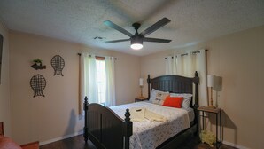 A bedroom with a bed, a ceiling fan, a bedside table with a lamp, and decorative wall art. - Lake Access, Firepit and Kayaks (Eucha)