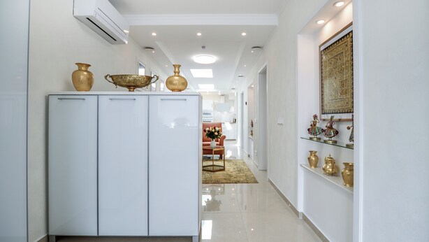 Un couloir avec une armoire blanche, une étagère en verre ornée d’objets décoratifs et un tapis à motifs.