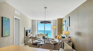 A modern hotel room with a dining area, a large window with a view, and a chandelier. - Hollywood Beach Retreat | Oceanview Resort (Hollywood)