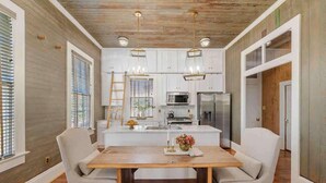 A modern kitchen with white cabinets, a central island, and pendant lighting. - As Seen On "Restoring Galveston": Rustic Luxury (Galveston)