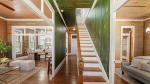 A spacious interior with a wooden staircase, a dining area, and a living room with a sofa. - As Seen On "Restoring Galveston": Rustic Luxury (Galveston)