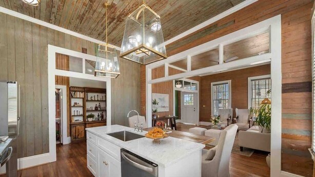 A spacious kitchen with a central island, wooden beams on the ceiling, and a dining area with a white sofa and chairs. - As Seen On "Restoring Galveston": Rustic Luxury (Galveston)