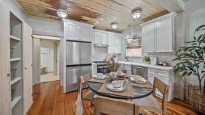 A modern kitchen with white cabinets, stainless steel appliances, and a dining area with a round table and chairs. - As Seen on "Restoring Galveston": Surf Shack (Galveston)