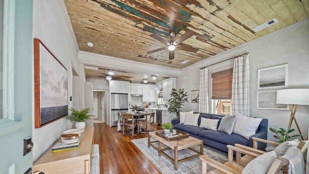 A spacious living room with a dark blue sofa, wooden coffee table, and a dining area with a wooden table and chairs. - As Seen on "Restoring Galveston": Surf Shack (Galveston)