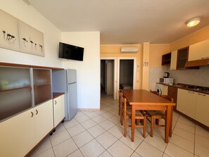 A kitchen with a dining table, chairs, a refrigerator, a microwave, and a TV mounted on the wall. - Peaceful Stay Near the Beach in Rosolina Mare (Rosolina)