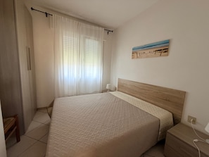 A bedroom with a bed, a nightstand, a wall-mounted painting, and a window with sheer curtains. - Peaceful Stay Near the Beach in Rosolina Mare (Rosolina)