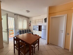 A compact kitchen with a dining table and chairs, a refrigerator, and a window with curtains. - Peaceful Stay Near the Beach in Rosolina Mare (Rosolina)