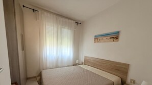 Une chambre à coucher avec un lit, une table de chevet, une lampe, un tableau au mur et une fenêtre avec des rideaux.