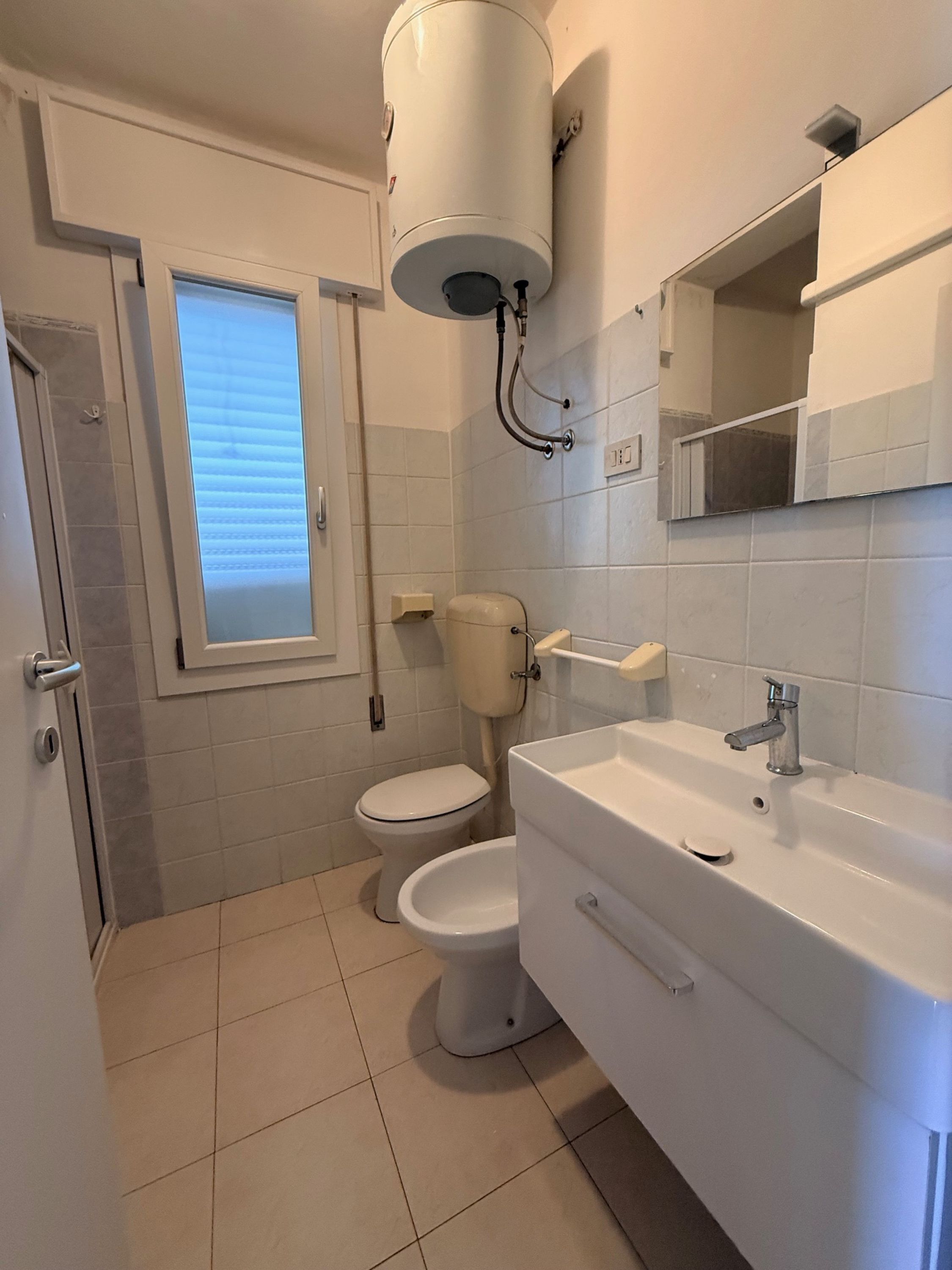 A bathroom with a toilet, bidet, sink, and a window.