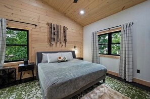 A bedroom with a bed, a desk, a chair, a window, and a wall-mounted light fixture. - 5-Bedroom Cabin with Glow Pool, Arcade Loft & Hot Tub, Sleeps 12 (Sevierville)