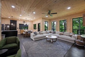 A modern interior with a large L-shaped sectional sofa, a dining area, and a kitchen. - 5-Bedroom Cabin with Glow Pool, Arcade Loft & Hot Tub, Sleeps 12 (Sevierville)