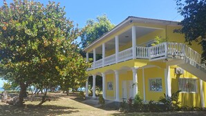 A yellow building with a balcony, surrounded by trees and a view of the sea. - Tropikal Apartments B (Aldea de Perú)