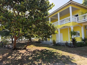 A yellow building with a balcony, surrounded by trees and a grassy area.
