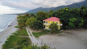 A yellow building with a red roof, surrounded by lush greenery and a beach. - Tropikal Apartments B (Aldea de Perú)