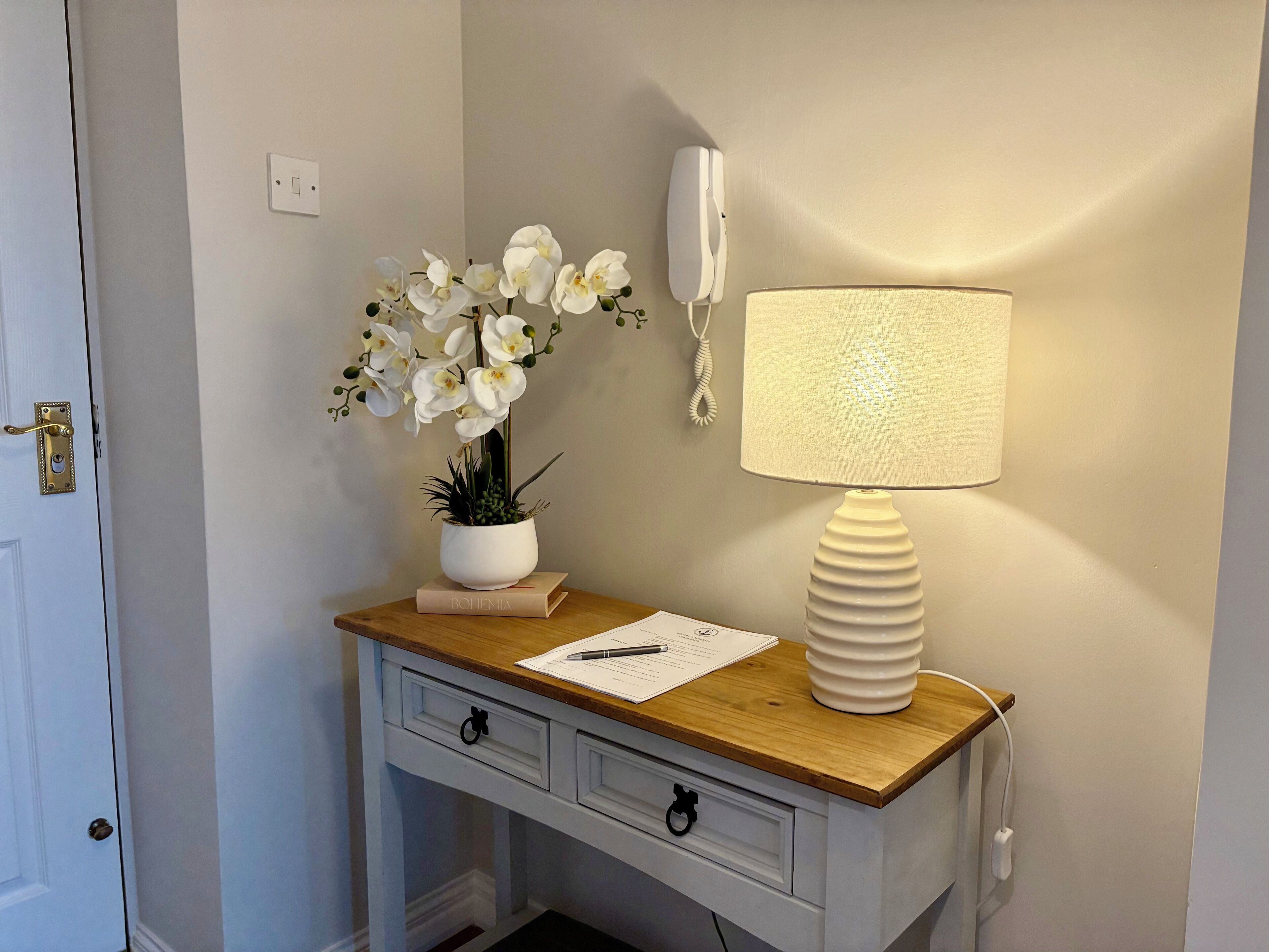 Un bureau avec une lampe, un téléphone, une plante et un bloc-notes.
