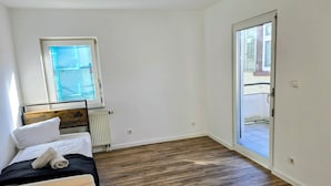 A bedroom with a wooden floor, a bed with white linens, a radiator, and a window.