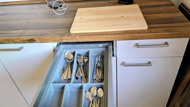 A kitchen with a wooden countertop, a cutting board, and a drawer organizer with utensils.