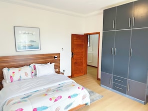 A bedroom with a bed, a wooden headboard, a framed picture on the wall, and a wardrobe.