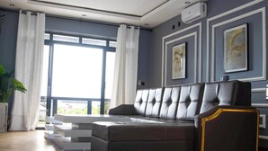 A modern living room with a sectional sofa, large windows with curtains, and framed artwork on the walls. - K&K Luxurious Landing (Limbe)